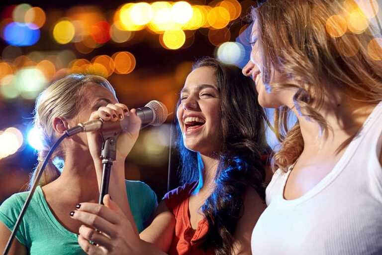 party, holidays, celebration, nightlife and people concept - happy young women singing karaoke in night club